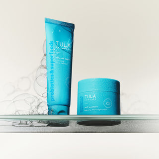 Tula skincare products on a glass shelf with water droplets.
