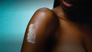 Close-up of a person's shoulder with body scrub applied against a blue gradient background