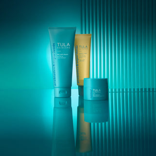 Three Tula skincare products on a reflective surface with a teal gradient background