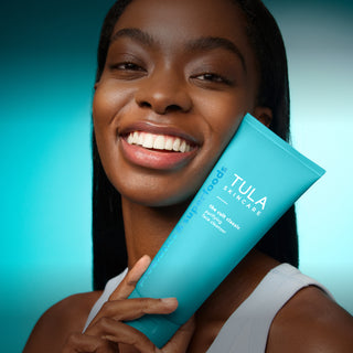 Woman holding a Tula skincare product against a gradient blue background