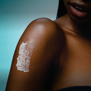 Close-up of a person's shoulder with body scrub applied against a blue gradient background