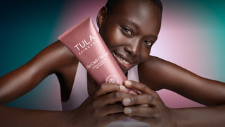 Woman holding a Tula Skincare product with a colorful gradient background