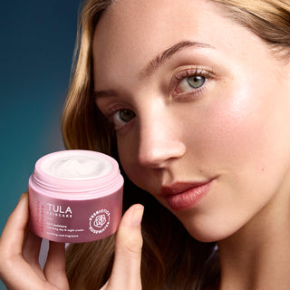 Woman holding a pink Tula Skincare jar with a blue gradient background