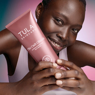 Woman holding a Tula Skincare product against a pink background