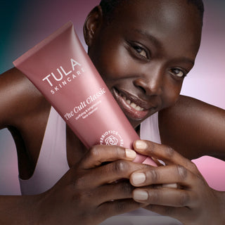 Person holding a Tula Skincare product with a pink background