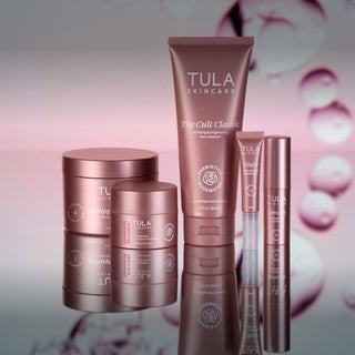 Tula Skincare products including a tube, jars, and a bottle on a reflective surface with a blurred background.