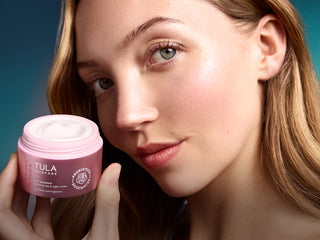 Woman holding a Tula skincare product with a blue gradient background