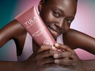 Person holding a Tula Skincare product with a colorful gradient background