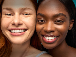 Two women with bright smiles, one with red hair and the other with dark hair, against a teal background.
