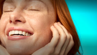 Close-up of a woman with red hair holding her ear against a blue background