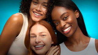 Three women with different hair colors smiling against a blue background