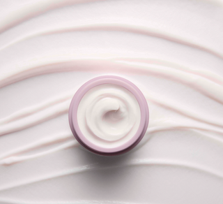 Close-up of a swirl of white cream with a purple rim on a light pink background