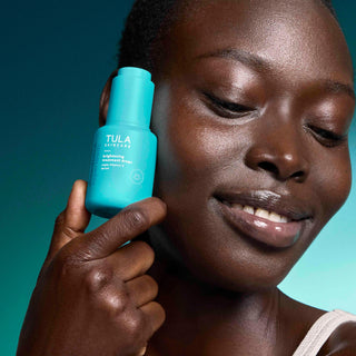 Woman holding a Tula skincare bottle against a teal background