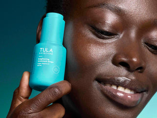 Person holding a Tula skincare product close to their face against a teal background