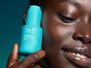 Person holding a blue Tula skincare bottle close to their face against a teal background