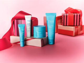 Tula skincare products on a pink background with red gift boxes.