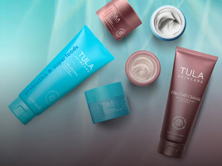 A flat-lay arrangement of Tula Skincare products on a soft teal gradient background.