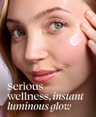 Woman applying cream to her face with text 'Serious wellness, instant luminous glow'.