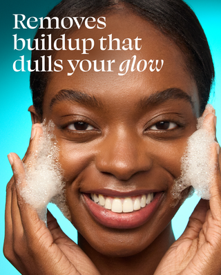 Woman cleaning her face with soap and water against a blue background with text that reads "Removes buildup that dulls your glow"