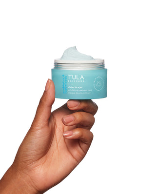 TULA Detox in a Jar Exfoliates and helps even the appearance of skin texture. Model holding product in hand.