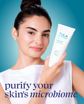 Woman holding a Tula skincare product against a blue background with text promoting skin microbiome.