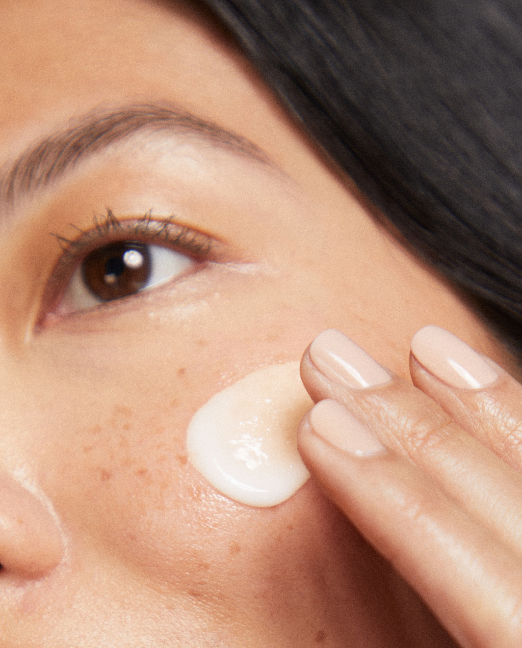 Close-up of a person applying cream under their eye with a finger.