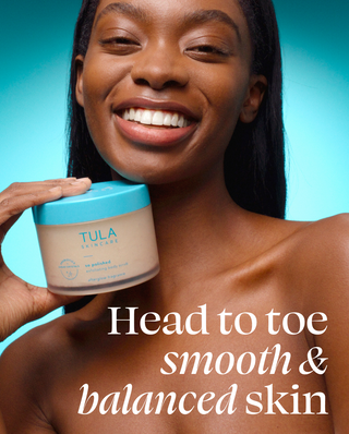 Woman holding TULA sugar scrub in front of teal background. 