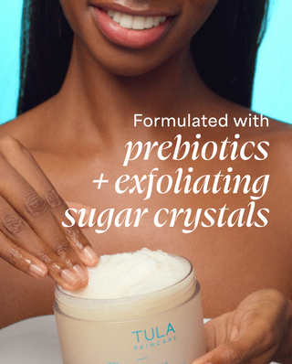 Woman holding TULA sugar scrub in front of teal background. 