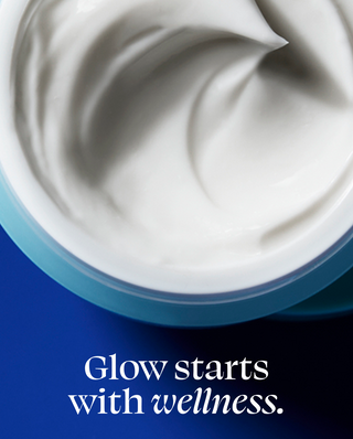 A close-up of a white cream or balm swirled inside a round container with a light blue rim, set against a dark blue background with the text 'Glow starts with wellness.'.