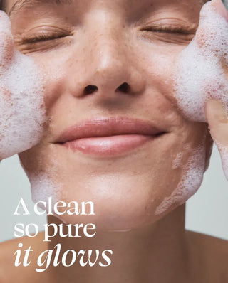 Person washing their face with soapy hands and text 'A clean so pure it glows' on a light background