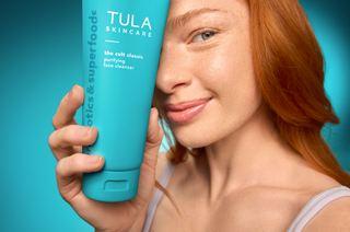 Woman holding a Tula skincare product against a blue background