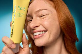 Woman holding a Tula skincare product against a blue background