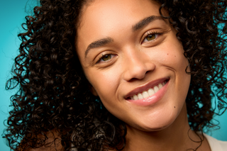 Woman with curly hair smiling against a blue gradient background