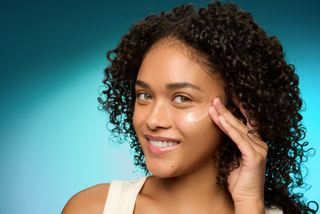 Model applying product to face with blue background. 